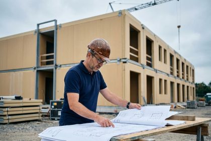 Architecte spécialisé en bâtiment modulaire examinant des plans sur un chantier de construction préfabriquée