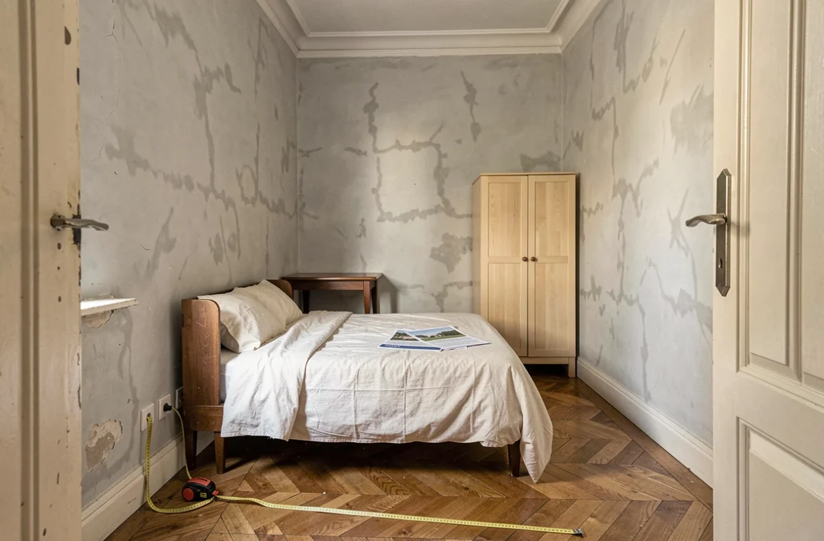 Petite chambre de moins de 9m2 dans un appartement parisien avec mètre ruban et documents réglementaires sur le lit